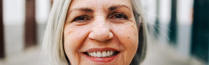Happy senior woman looking at camera with city on background. Latin american older community concept